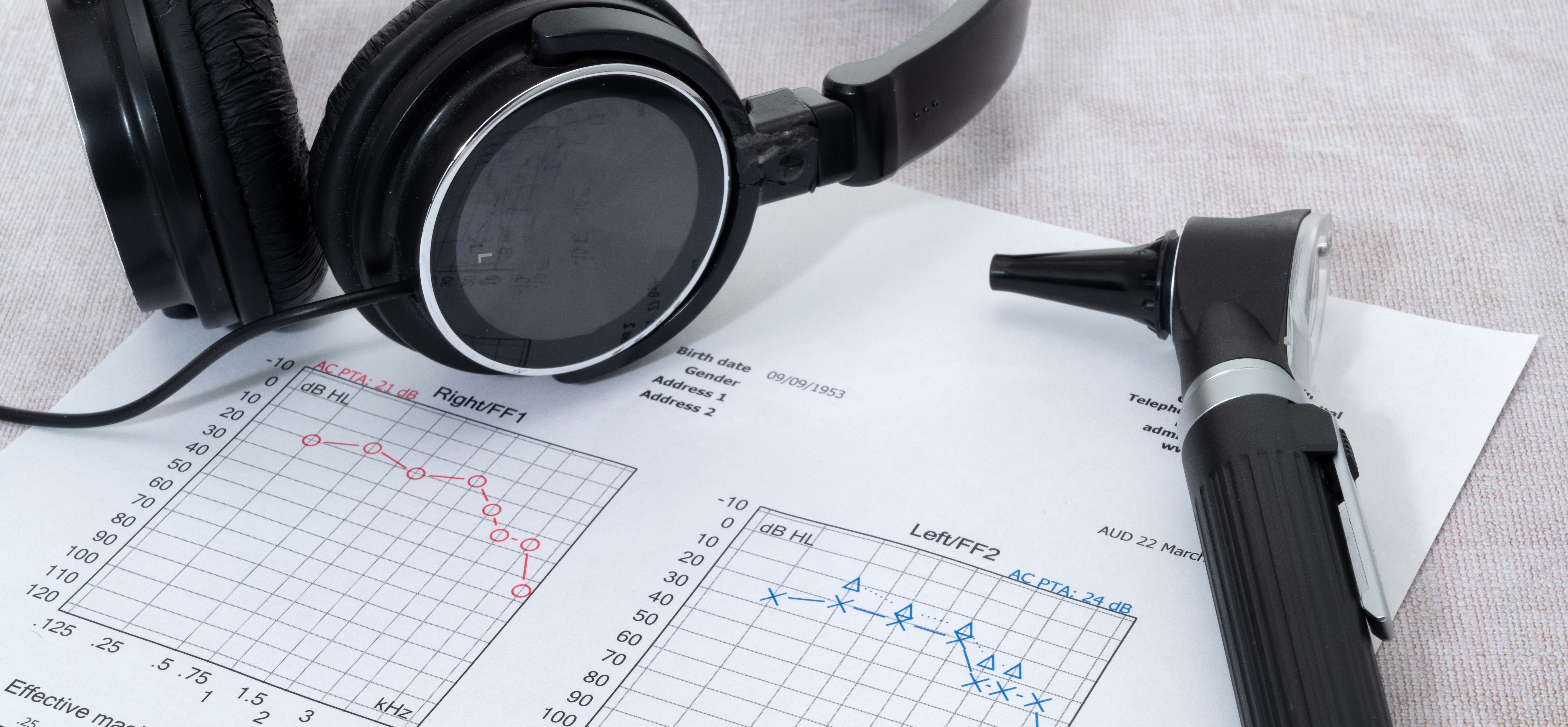 An otoscope and a pair of headphones rest on a printed audiogram