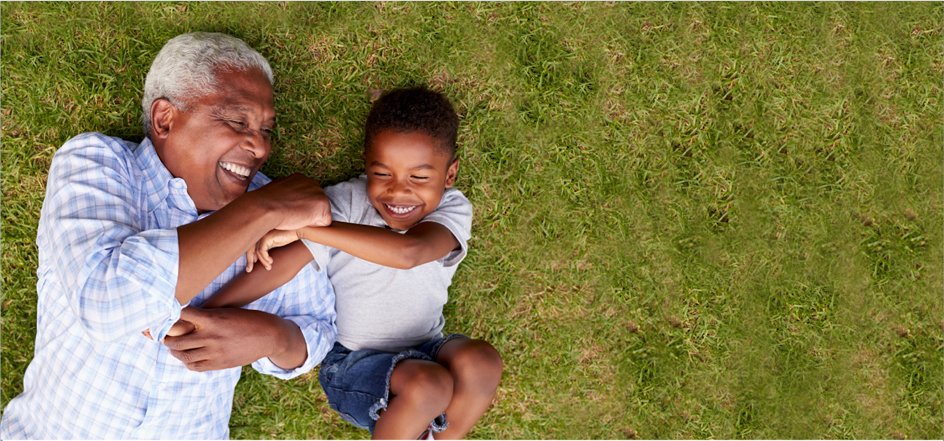 An older man and a young boy are laying on the grass and playing