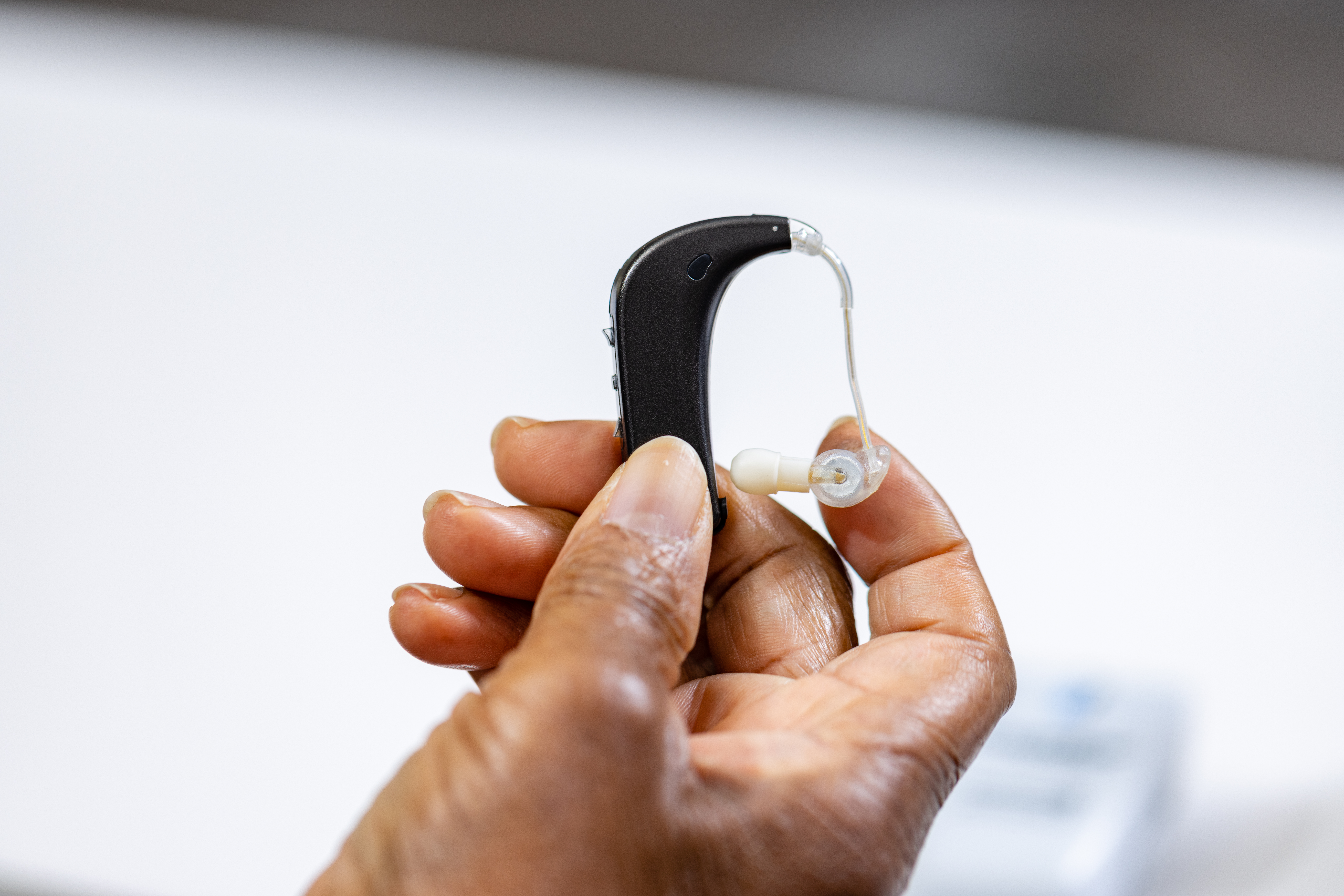 A right hand holding a simple hearing device.