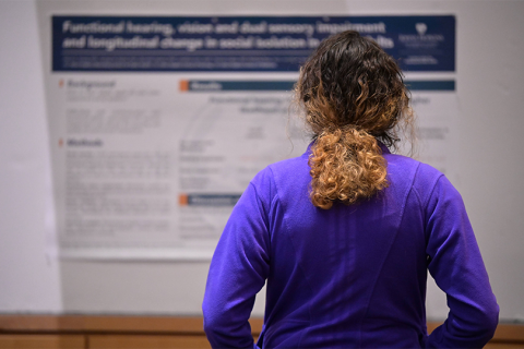 Photo of a person in the foreground looking a college presentation poster in the background