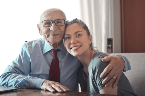 An older man wearing a tie has his arm around a younger woman