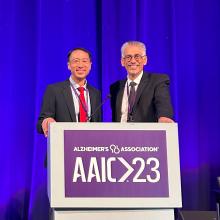 Frank Lin and Joe Coresh stand behind a podium before presenting ACHIEVE trial results at the AAIC in Amsterdam, July 2023