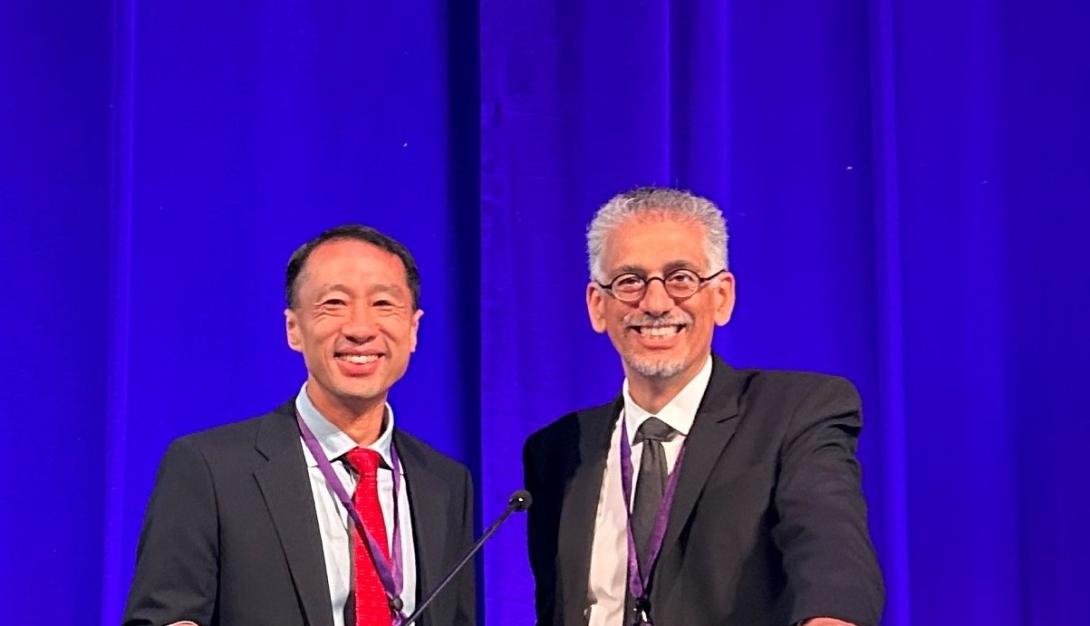 Frank Lin and Joe Coresh stand behind a podium before presenting ACHIEVE trial results at the AAIC in Amsterdam, July 2023